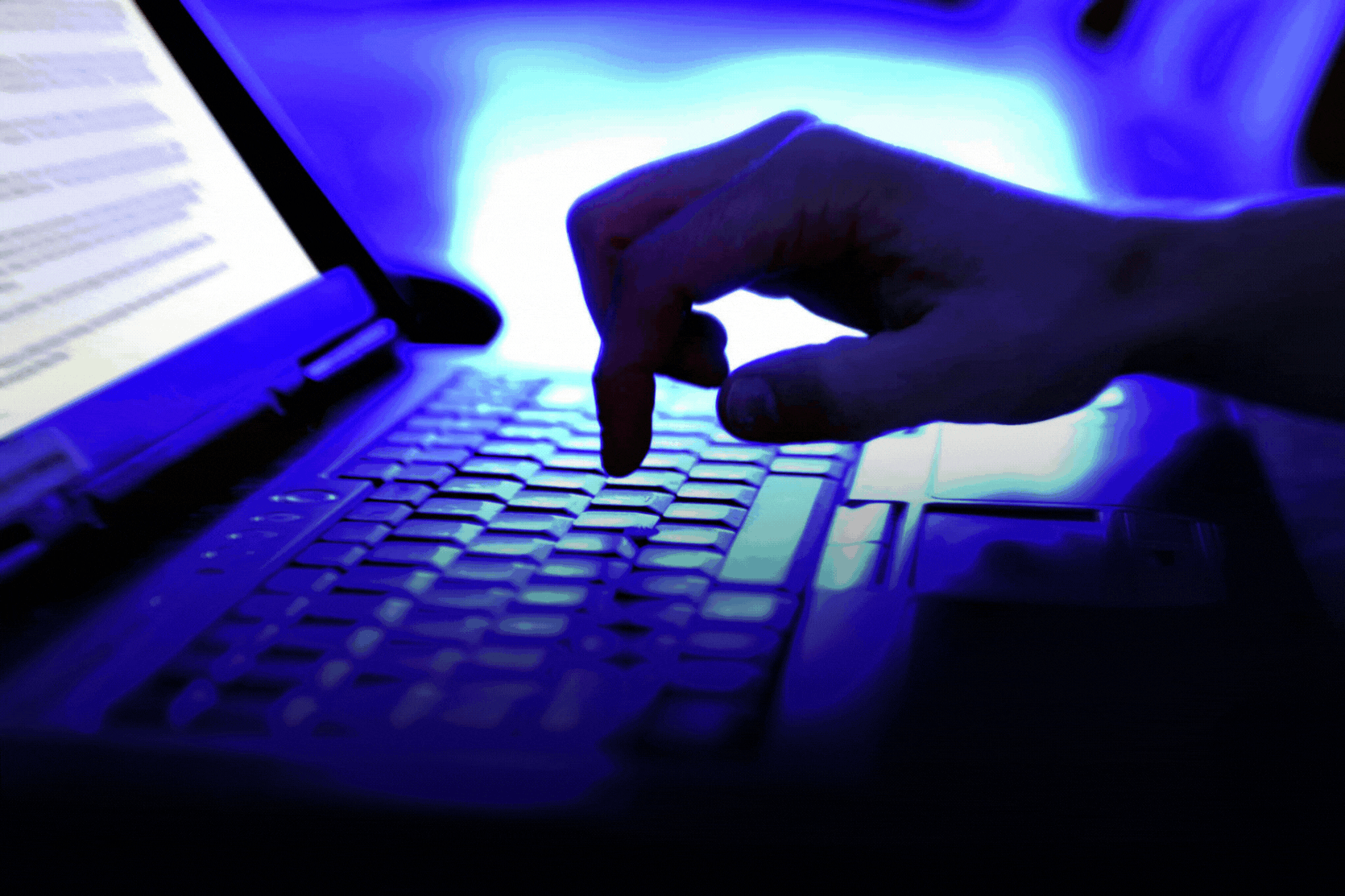 Escribir a mano en el teclado de la computadora portátil con el documento de texto abierto en la pantalla iluminada por luz azul. Tenga cuidado al moverse en línea para evitar ser víctima de perfiles falsos y esquemas de estafadores ocultos.