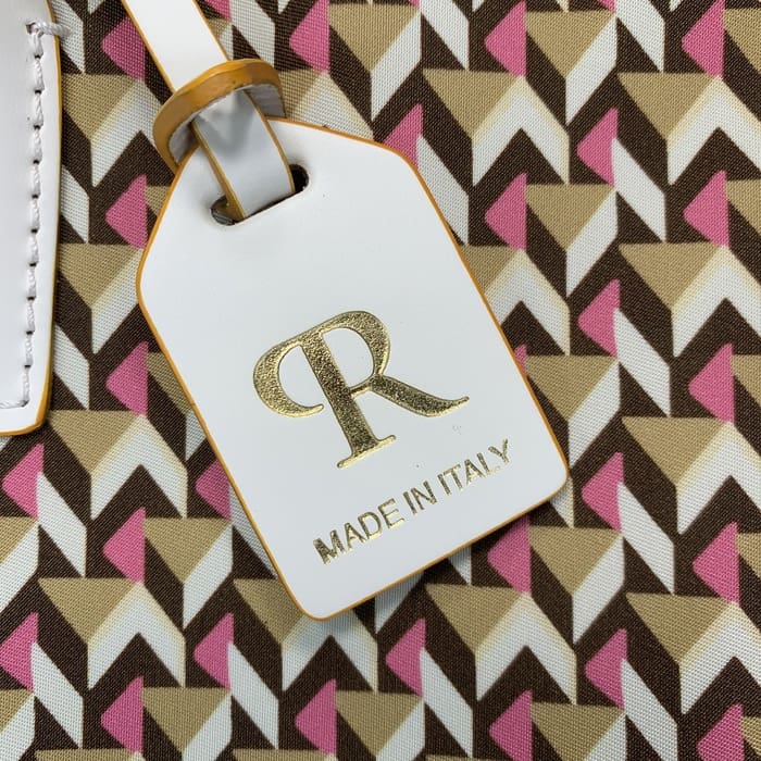Un primer plano de una etiqueta de equipaje blanca de Roberta Pieri con la letra "R" en oro y las palabras "MADE IN ITALY" unidas a una mini bolsa de lona con patrones geométricos marrones, beige y rosas.