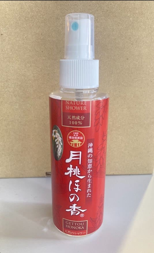 Una botella de spray roja con las palabras "Nature Shower" escritas sobre un fondo beige. Boquilla y tapón de pulverización blancos.