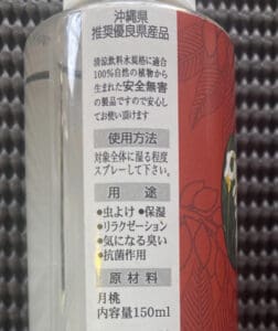 円筒形のボトルのクローズアップ。ラベルには日本語の文字があり、沖縄の月桃をイメージした赤と花の装飾模様が描かれている。ボトルには150mlの液体が入っており、製品情報と使用方法が記載されている。.