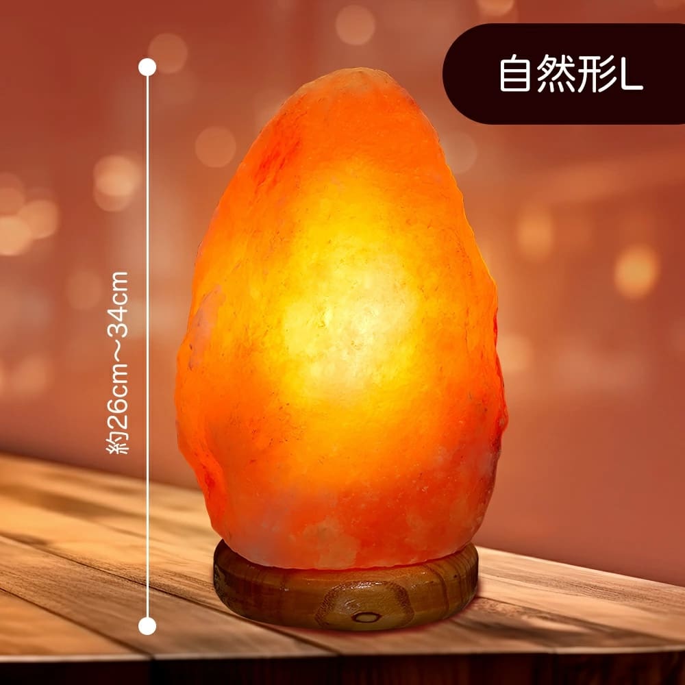 オレンジ色に輝く天然岩塩ランプ【サイズ：SS】— ほっと落ち着く、優しい間接照明 — 木製の台座がテーブルの上に置かれ、柔らかな間接照明を放っています。日本語の文字と白い縦線で高さ（約26cm〜34cm）が示されています。背景は温かみのある照明で柔らかくぼかされています。.
